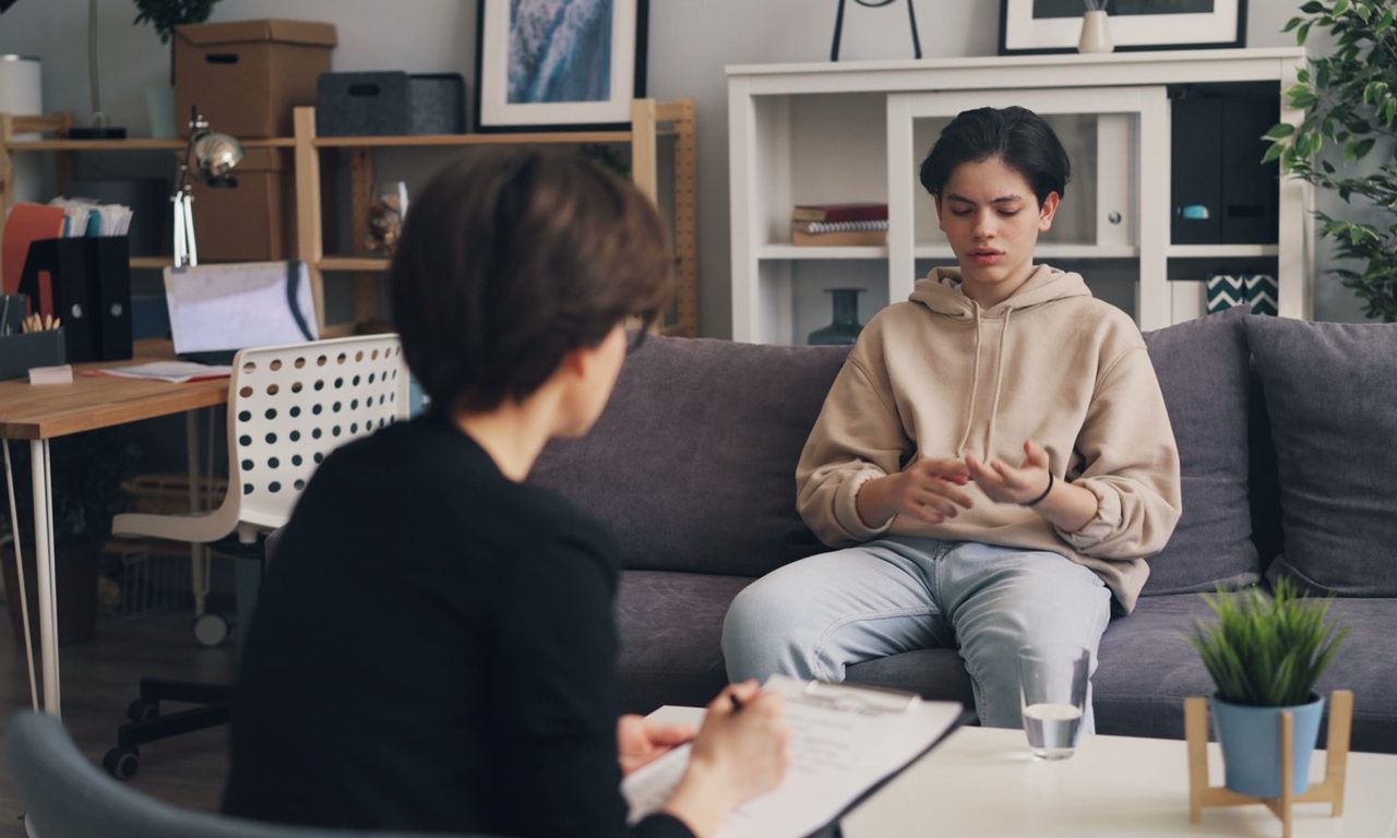 Therapeutische Sitzung in einem hellen Raum: eine Person macht Notizen, die andere sitzt auf dem Sofa und spricht